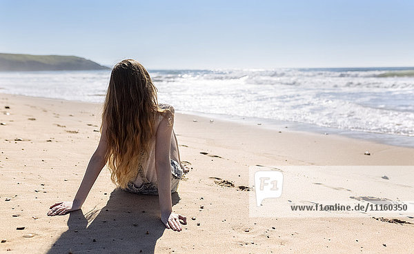 Back view of teenage girl sitting on the beach