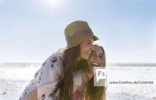 Teenage girl giving her best friend a piggyback ride on the beach