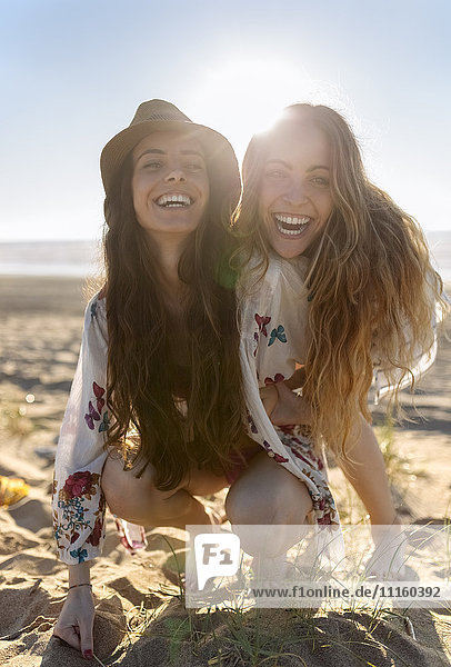 Portrait of two best friends crouching on the beach at backlight