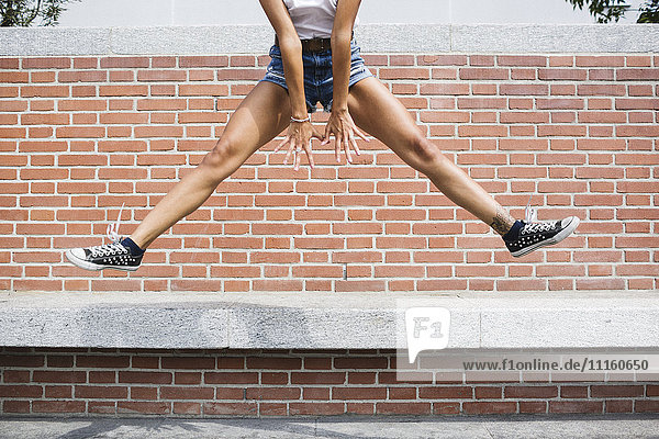 Low section of woman in hot pants jumping at brick wall