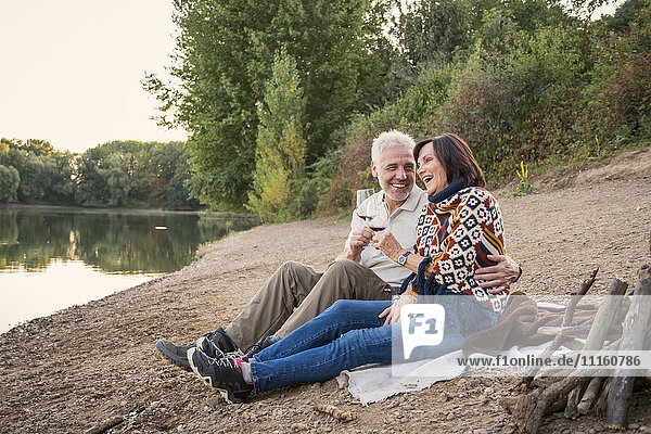 Happy senior couple with wine at a lake in the evening