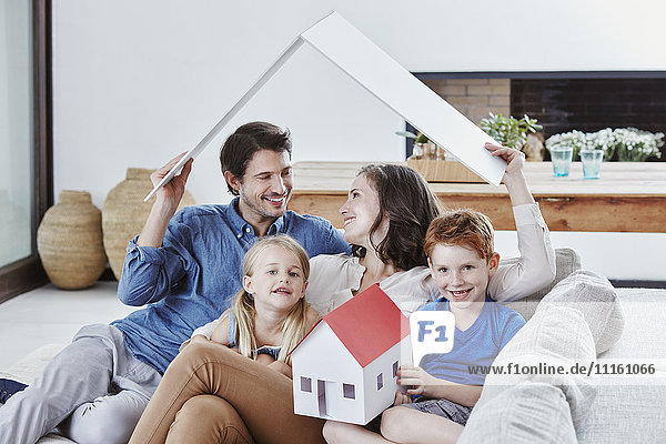 Glückliche vierköpfige Familie mit Hausmodell im Wohnzimmer