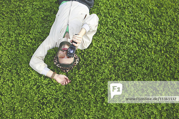 Young man lying on a meadow using a vintage video camera