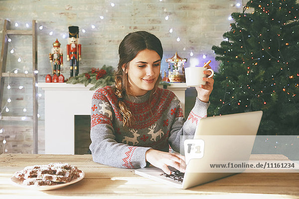 Lächelnde Frau mit Tasse Kaffee mit Laptop zur Weihnachtszeit