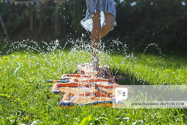 Girl jumping on inflatable water cushion in the garden  partial view