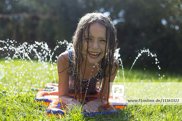 Porträt des lachenden Mädchens mit aufblasbarem Wasserkissen im Garten