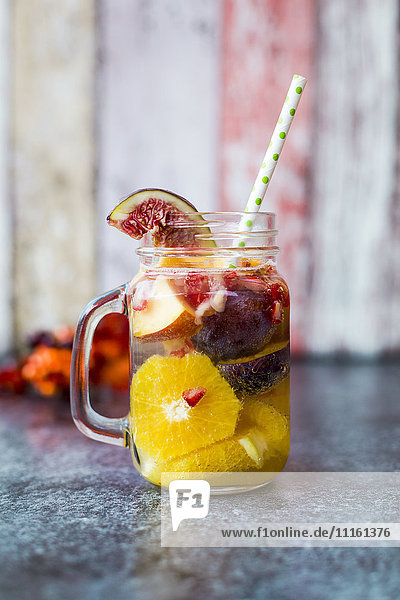 Glass of infused water with orange slices  fig  pomegranate seed  nectarine and plums