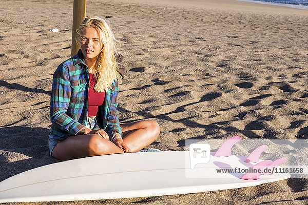 Spanien  Teneriffa  junge blonde Surferin am Strand sitzend
