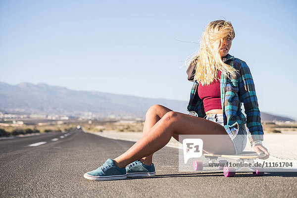 Spanien  Teneriffa  blonde junge Skaterin auf dem Skateboard sitzend