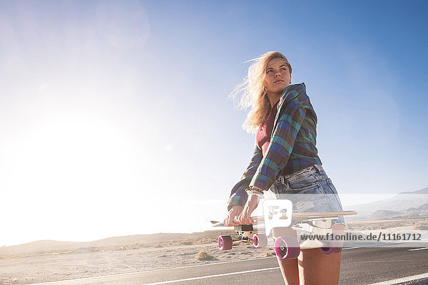 Spanien  Teneriffa  blonde junge Skaterin mit Skateboard gegen die Sonne