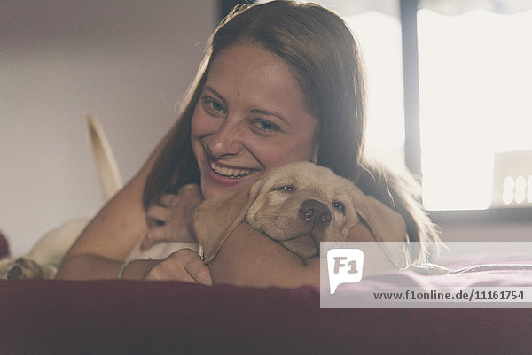 Porträt einer glücklichen jungen Frau  die ihren Labrador Retriever Welpen kuschelt.