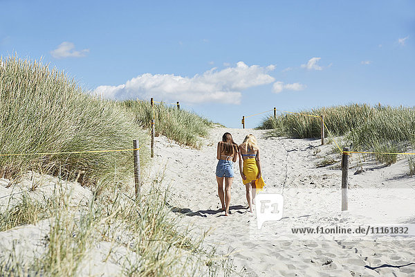 Two female friends walking through dunes leaving beach
