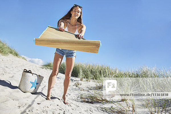 Junge Frau beim Ausbreiten der Strandmatte am Strand
