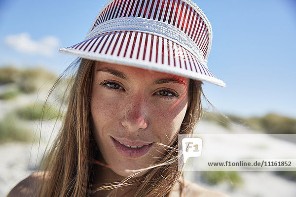 Porträt einer lächelnden jungen Frau mit Sonnenblende am Strand