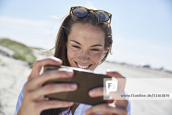 Lächelnde junge Frau mit Handy am Strand