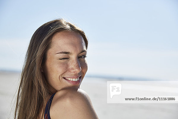Lächelnde junge Frau funkelt am Strand