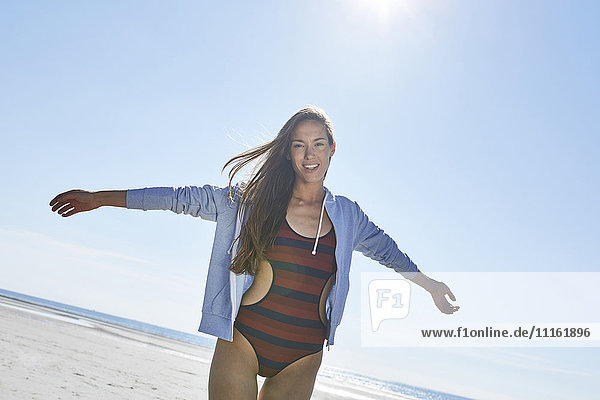 Fröhliche junge Frau mit ausgestreckten Armen am Strand