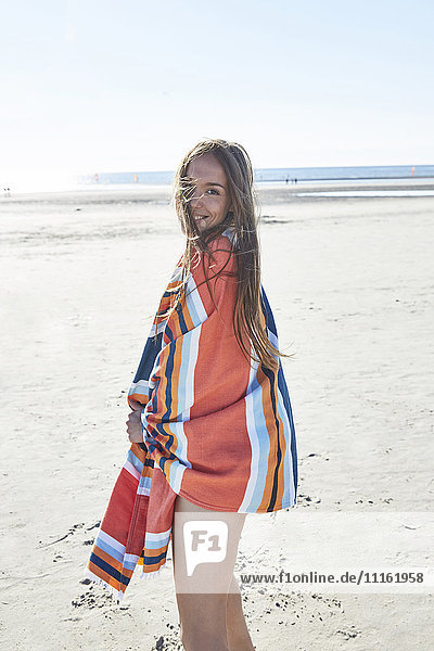 Smiling young woman wrapped in a blanket on the beach