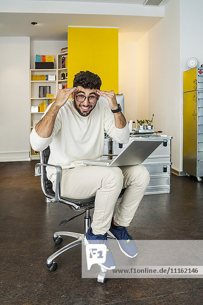 Young man with laptop in a modern office pulling funny faces