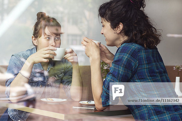 Zwei Frauen sitzen hinter der Fensterscheibe eines Cafés und trinken Kaffee.