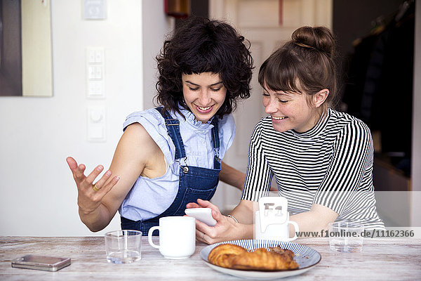 Two women at breakfast table looking together at smartphone