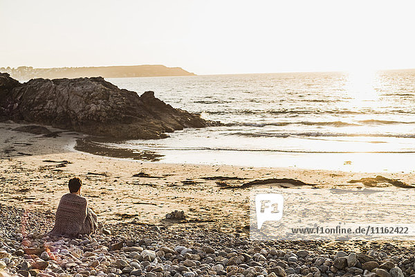 Frankreich  Halbinsel Crozon  Frau bei Sonnenuntergang am Strand sitzend