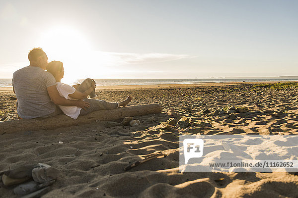 Frankreich  Bretagne  Finistere  Halbinsel Crozon  Paar am Strand sitzend  Sonnenuntergang genießen
