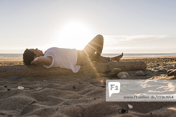 Frankreich  Bretagne  Halbinsel Crozon  Frau auf Baumstamm liegend  Strand bei Sonnenuntergang