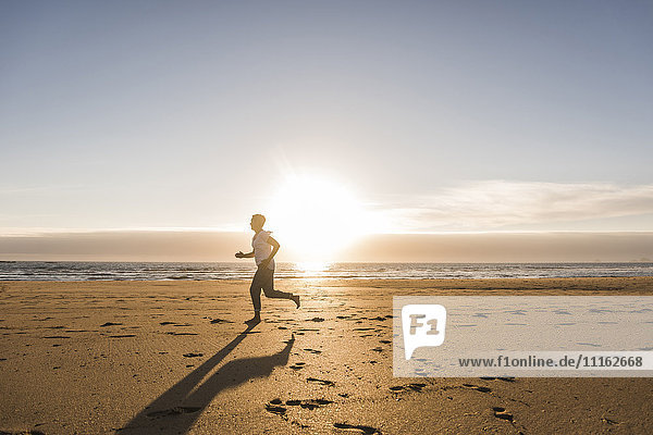 Frankreich  Bretagne  Halbinsel Crozon  Frau läuft am Strand bei Sonnenuntergang