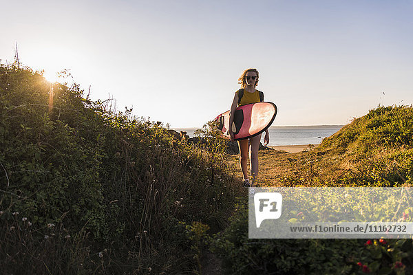 Teenage girl on the beach carrying surfboard