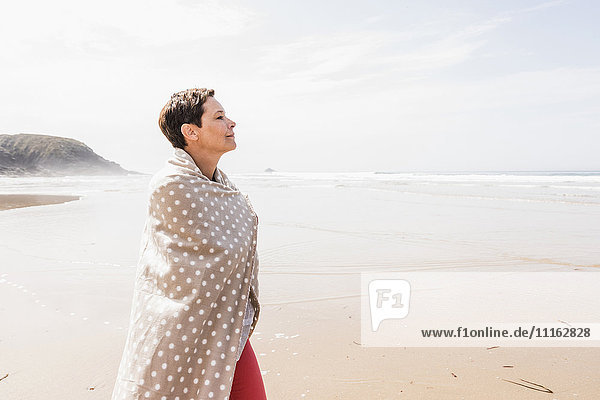 Mature woman wrapped in a blanket on the beach