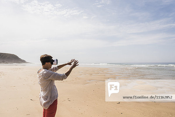 Reife Frau am Strand stehend mit VR-Brille