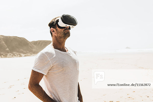 Mature man standing on the beach wearing VR glasses