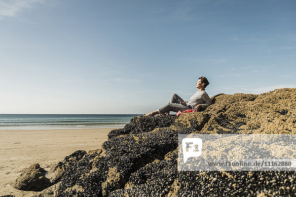 Reife Frau entspannt sich am Strand auf dem Felsen