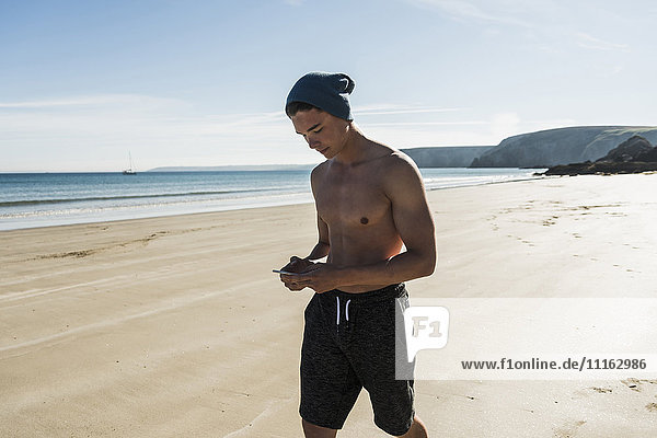 France  Crozon peninsula  young man with cell phone walking on the beach