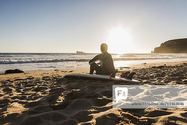 France  Bretagne  Crozon peninsula  woman sitting on beach at sunset with surfboard