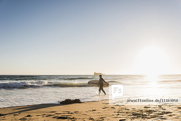 Frankreich  Bretagne  Halbinsel Crozon  Frau im Meer bei Sonnenuntergang mit Surfbrett