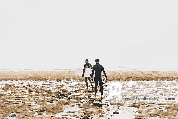 France  Bretagne  Crozon peninsula  couple walking on beach carrying surfboards