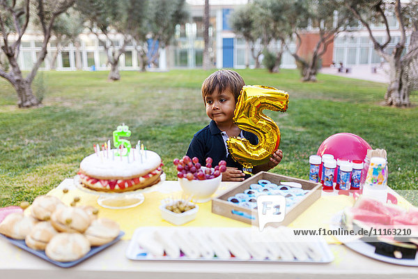 Kleiner Junge mit goldenem Ballon hinter gedecktem Geburtstagstisch