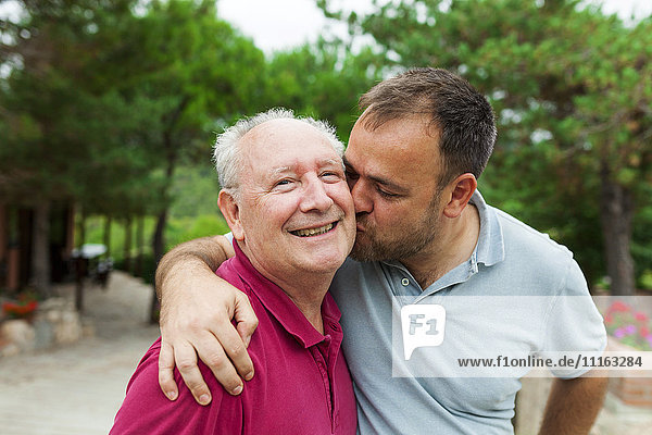 Adult son kissing and hugging his old father
