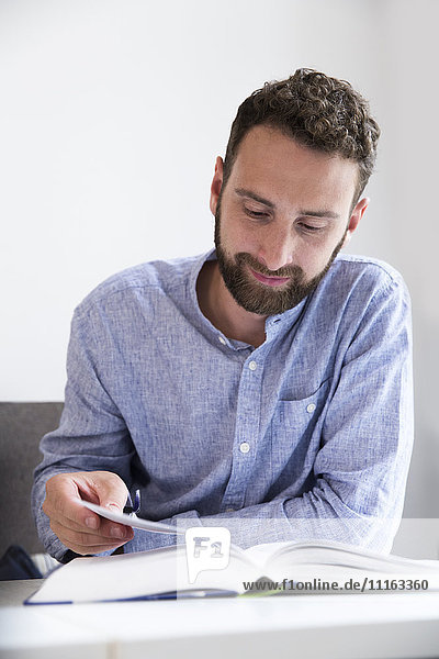 Junger Mann beim Lesen eines Buches am Tisch