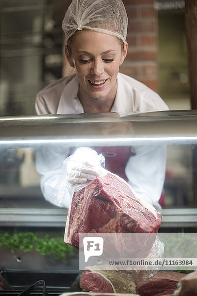 Woman putting meat on display in butchery