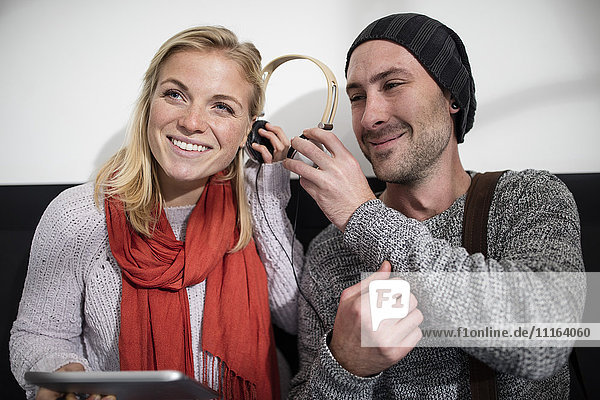 Junger Mann teilt Kopfhörer mit junger Frau