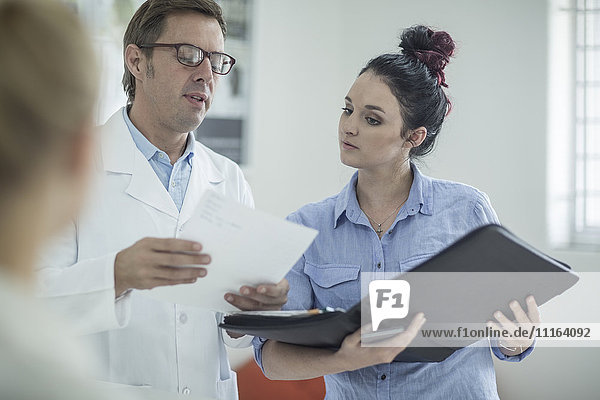 Man in lab coat talking to woman holding folder