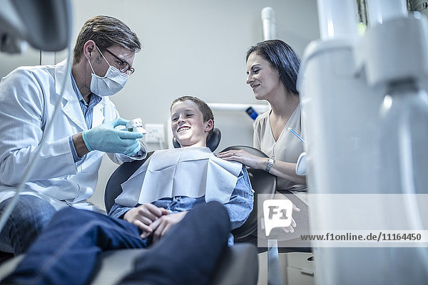 Kieferorthopäde erklärt dem Jungen mit der Mutter in der Zahnarztpraxis die Zahnform.
