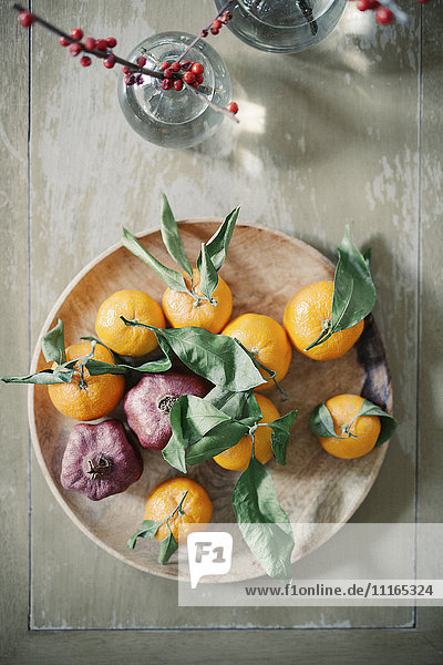 Eine Holzschale mit Orangen,  Zitrusfrüchten auf einer Tischplatte.