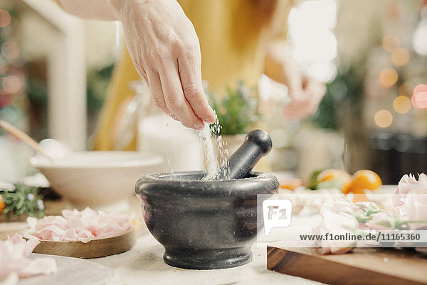 A hand adding ingredients to a pestle and mortar on a kitchen counter.