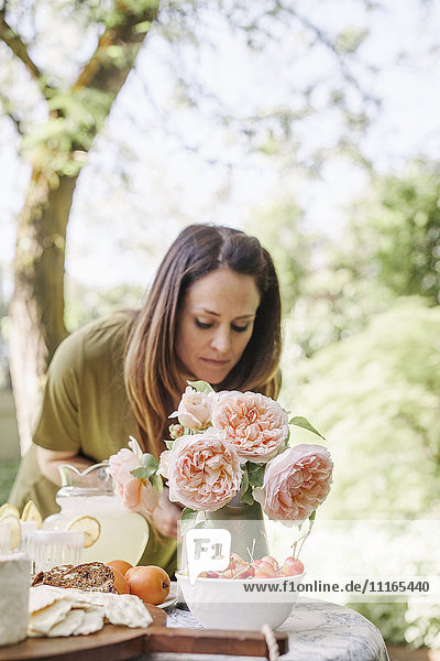 Frau  die an einem Tisch in einem Garten steht  eine Vase mit rosa Rosen und eine Schale mit Kirschen.