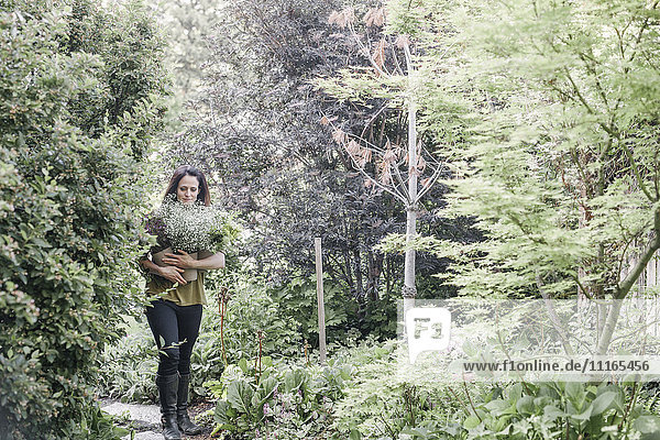 Frau  die durch einen Garten geht und einen großen Blumenstrauß trägt.