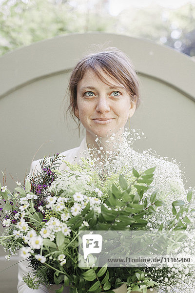 Porträt einer lächelnden Frau  die einen weißen Blumenstrauß trägt.